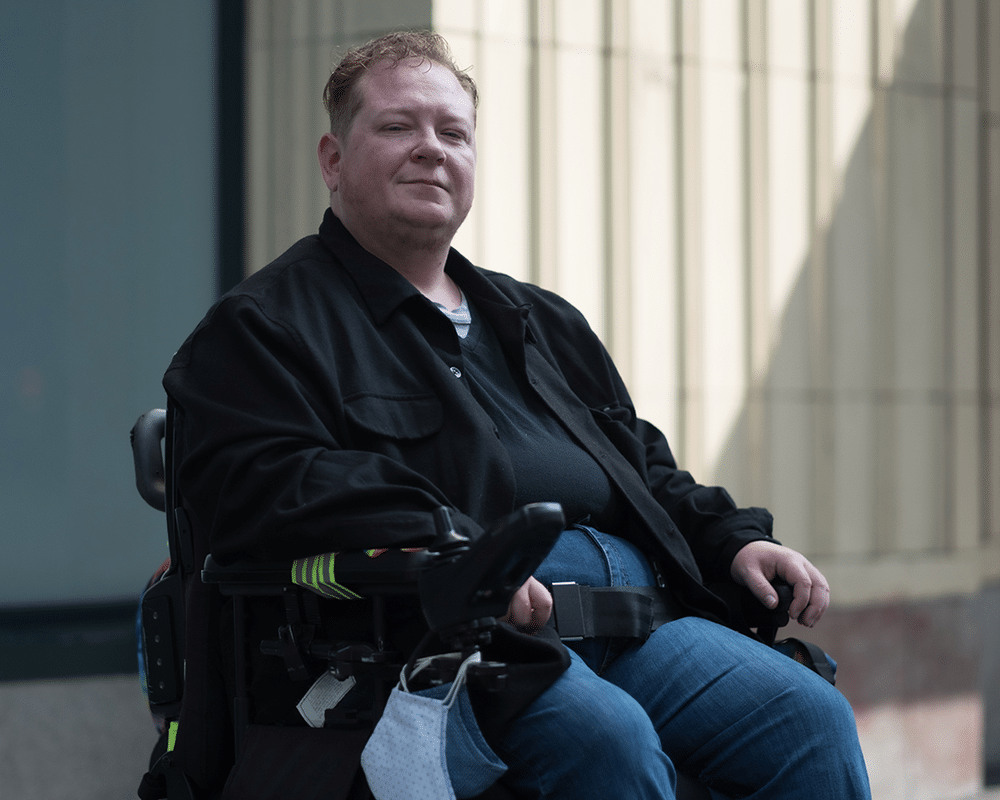 A trans man sitting in his powerchair, smiling