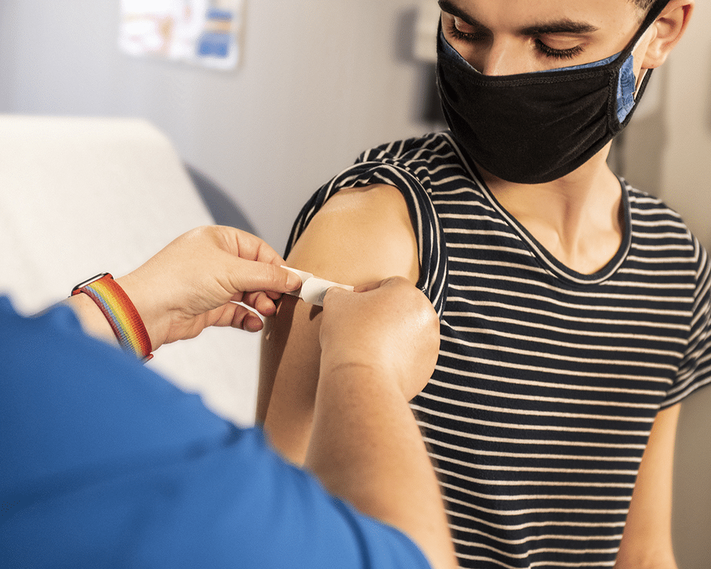 A person sitting with their sleeve rolled up, as a nurse puts a band aid on their arm