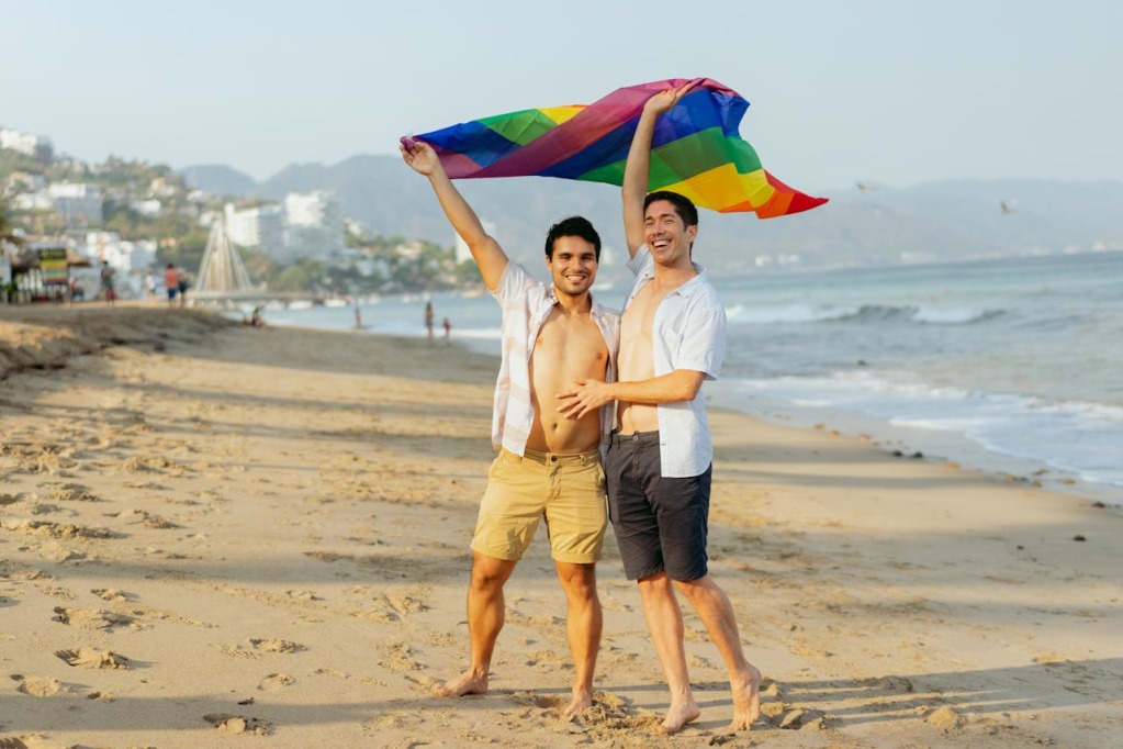 Two men holding a rainbow flag on a beach. Picture by Cristian Rojas.